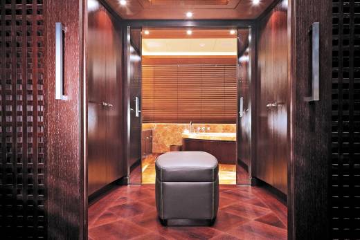 Step into a luxurious bathroom through a richly paneled hallway, complete with a plush ottoman.
