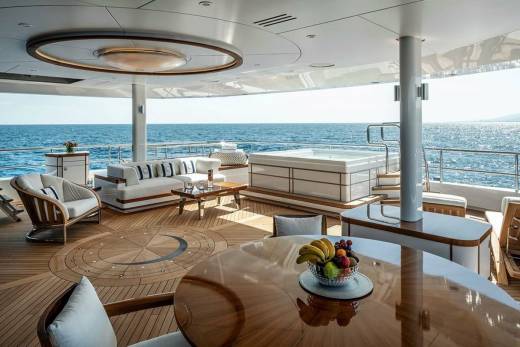 Luxurious yacht deck offers a serene oasis with a hot tub, plush seating, and a fruit-laden dining table overlooking the sparkling ocean.
