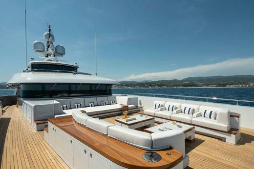 Luxurious white sofas and coffee tables create a stunning outdoor lounge on the deck of a yacht against a backdrop of the azure sea and distant hills.