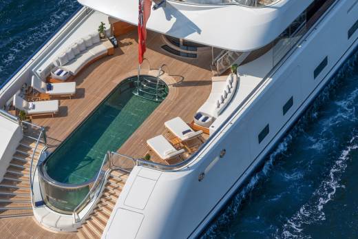 A luxurious yacht glides through the deep blue sea, its deck featuring a stunning swimming pool and ample space for sunbathing.