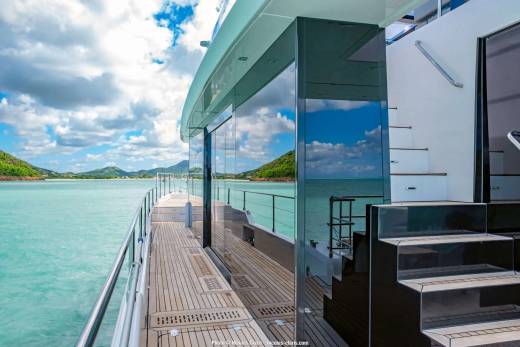Reflections of a brilliant blue sky and fluffy clouds dance on the sleek glass exterior of this luxurious yacht as it glides through turquoise waters.