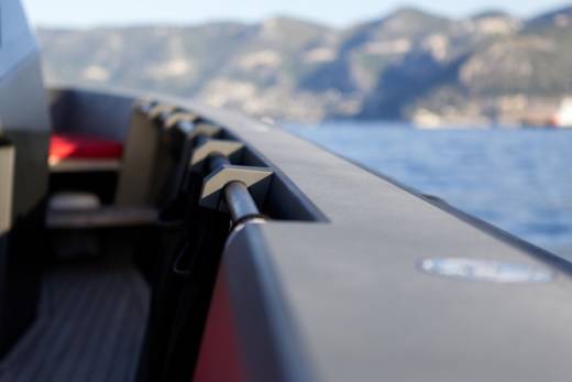 A sleek boat's railing offers a close-up perspective against a blurred backdrop of blue water and distant mountains.