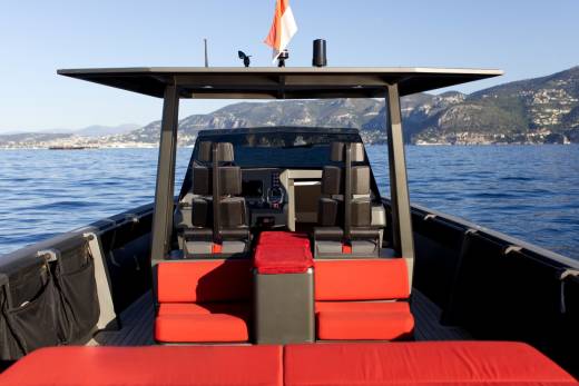The sleek interior of a modern yacht offers comfortable seating and a commanding view of the sparkling blue sea and distant mountains.