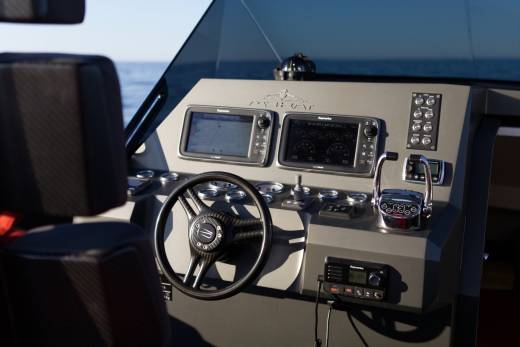 The helm of a sleek yacht features modern navigation displays and a carbon fiber steering wheel, ready for the open sea.