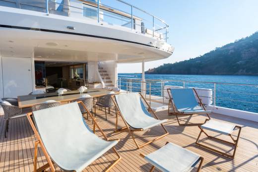 Relax on the spacious deck of a luxury yacht, enjoying the stunning coastal views under a clear blue sky.