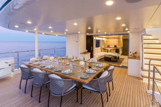 An elegant outdoor dining area on a yacht is set for a meal with the ocean as a backdrop.