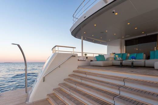 Luxurious yacht deck seating with turquoise cushions overlooks the serene ocean at sunset.
