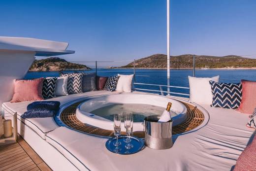 Champagne chills in an ice bucket beside flutes and towels on a luxurious yacht's sundeck overlooking a serene bay.