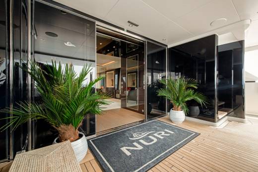 A welcome mat with the NURI logo sits on a teak deck outside a yacht's gleaming entrance.