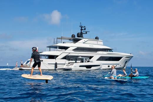 People enjoy various water sports near a large yacht on a sunny day.