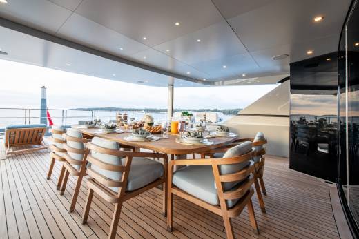 A beautifully set dining table awaits guests on the deck of a luxurious yacht, overlooking a serene coastal landscape.