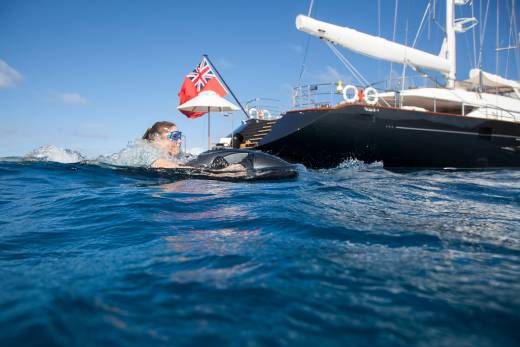 A woman enjoys a ride on a sea scooter near a large yacht flying the Red Ensign flag.