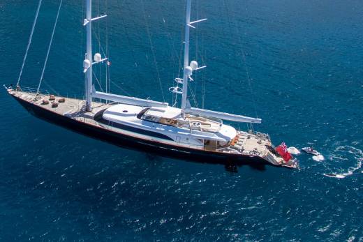 A majestic sailing yacht glides through the azure waters, accompanied by a jet ski and several towed watercraft.