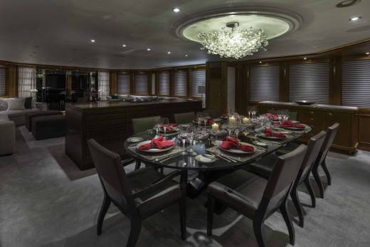 A lavish yacht dining room features a crystal chandelier illuminating a set table with red napkins and candles.