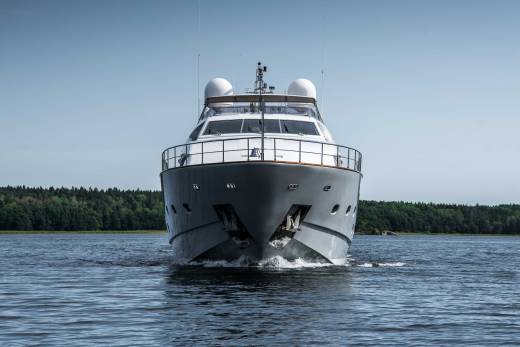A sleek grey yacht cuts through calm blue waters with a lush green forest lining the horizon.