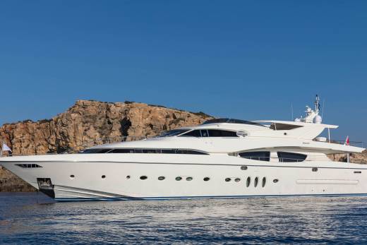 A sleek white yacht glides through calm blue waters against a backdrop of rugged, sun-drenched cliffs.