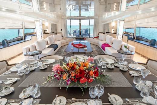 A beautifully set dining table aboard a luxury yacht awaits guests with a vibrant floral centerpiece and stunning ocean views.