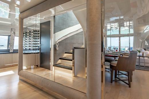 A luxurious yacht interior features a mirrored staircase, a well-stocked wine cellar, and a dining area with ocean views.