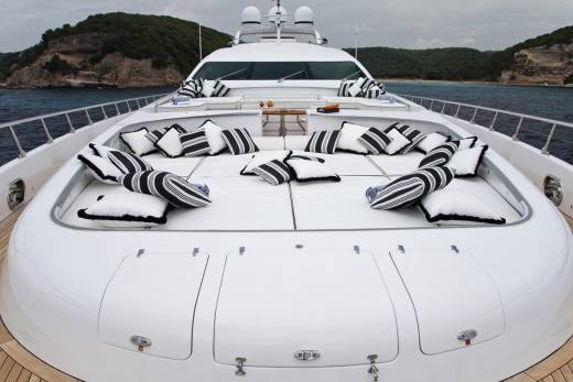 Luxurious yacht seating with striped pillows invites relaxation on the open water against a backdrop of rugged, green coastline.