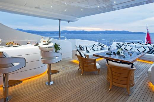 Luxurious yacht deck seating and bar area bathed in the warm glow of sunset over the tranquil sea.