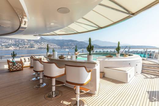 Luxurious bar stools and a jacuzzi await on this yacht's deck, offering stunning views of a coastal landscape.
