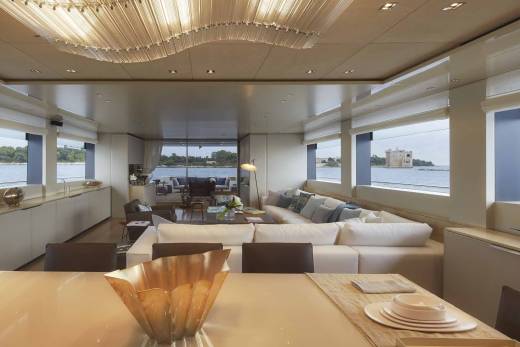 A luxurious yacht interior offers stunning ocean views and a comfortable seating area with a modern chandelier overhead.