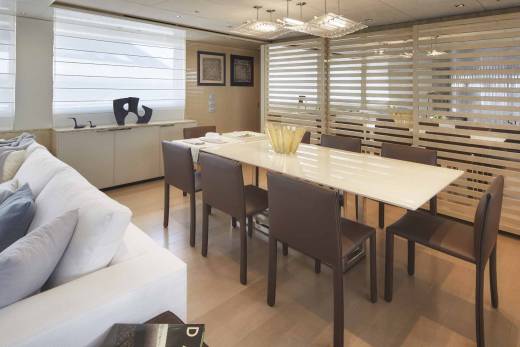 A modern dining room features a long table with brown chairs, a white sofa, and a decorative screen.