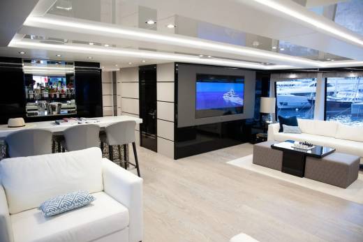 This luxurious yacht interior features a sleek bar, a large television displaying a yacht, and comfortable seating overlooking the water.
