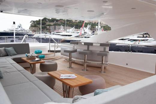 Luxurious yacht deck seating and bar area overlooks a harbor filled with impressive vessels.