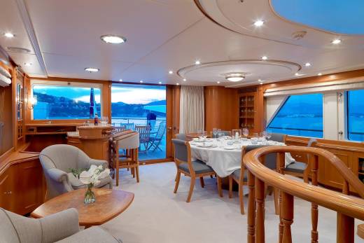 A luxurious yacht dining room opens to a serene twilight view of the sea and distant hills.