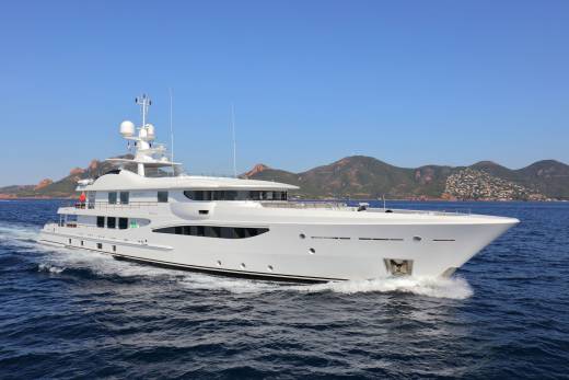 A sleek white yacht cruises through the deep blue sea with a picturesque mountainous coastline in the background.