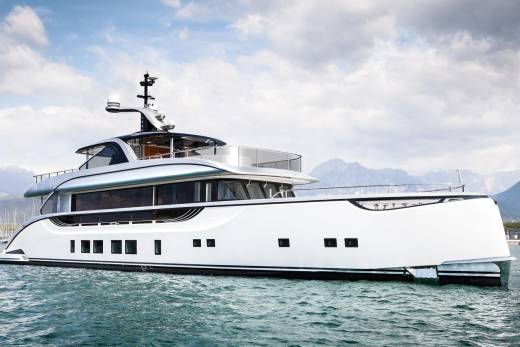 A sleek white superyacht glides through calm turquoise waters with majestic mountains in the background.