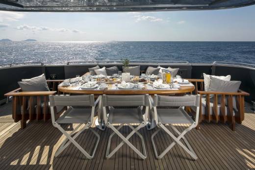 A beautifully set breakfast table awaits on the deck of a yacht, overlooking the sparkling blue ocean.