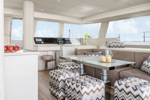 A modern yacht interior features a sleek dining area with a glass-topped table, plush seating, and panoramic windows overlooking the ocean.