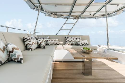 Relax on the plush seating of this luxury yacht's deck, complete with a wooden table and a bowl of fresh green apples.