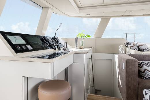 The modern yacht interior features a sleek helm station with advanced navigation screens and comfortable seating overlooking the bright blue sky.