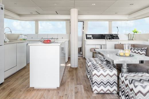 A modern yacht interior features a sleek white kitchen and a dining area with patterned seating.