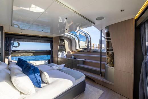 Luxurious yacht cabin offers stunning ocean views through expansive windows and a skylight, complemented by plush bedding and serene decor.