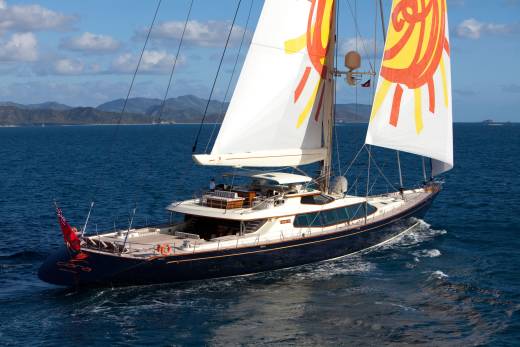 The majestic yacht Clara glides through azure waters, its vibrant sails catching the sun's rays against a backdrop of lush islands.