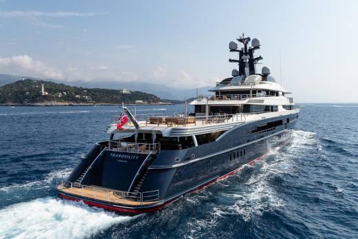 The luxurious superyacht Tranquility glides through the azure waters off a picturesque coastline dotted with lush green hills.