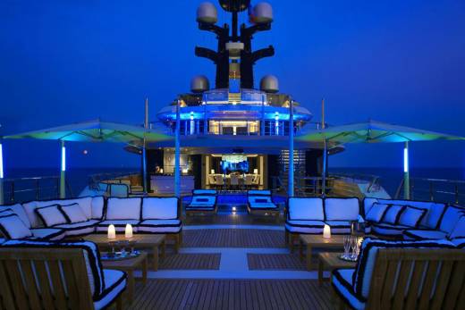 Luxurious yacht deck glows with blue lights and plush seating, inviting guests to enjoy a serene evening at sea.
