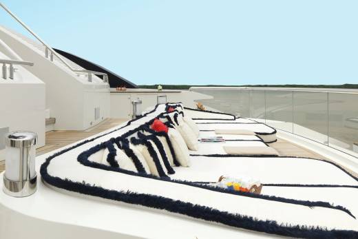 Luxurious white cushions with navy trim adorn the deck of a sleek yacht, inviting relaxation under a clear blue sky.