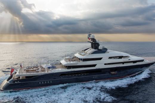 The luxurious superyacht Equanimity glides through the ocean under dramatic, sun-drenched clouds.
