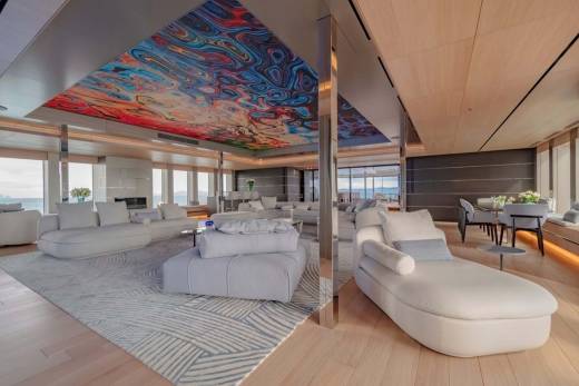 A luxurious yacht interior features a vibrant, abstract ceiling mural complementing plush white seating and expansive ocean views.
