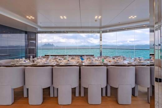 A beautifully set dining table awaits guests on a yacht, with panoramic windows offering stunning ocean views.