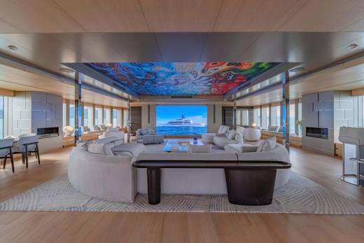 A luxurious yacht lounge features a massive screen displaying a ship at sea, complemented by a vibrant, abstract ceiling mural.
