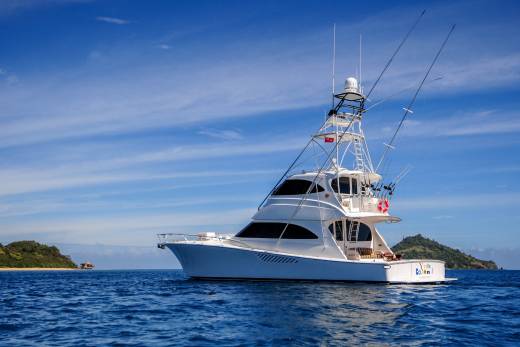 A sleek white yacht cruises through the deep blue ocean waters under a bright, cloudy sky.