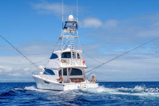 A luxurious sportfishing yacht cuts through the deep blue ocean under a bright sky with people fishing on deck.