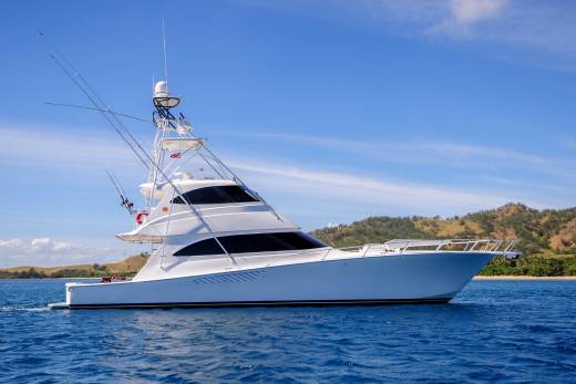A sleek white yacht cruises through the clear blue waters off a lush, tropical island.