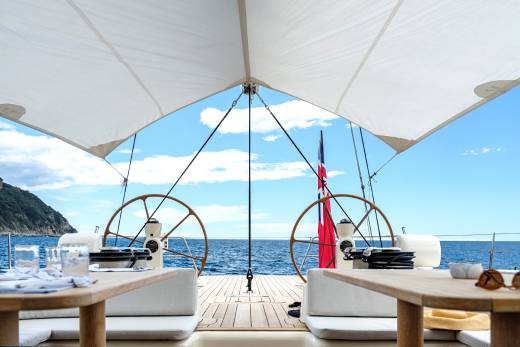 Enjoy a luxurious al fresco dining experience on deck with stunning ocean views and a backdrop of lush green hills.